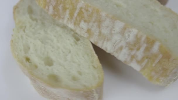 Färskt ekologiskt bröd i skivor staplade på en platta rotera på en vit bakgrund — Stockvideo