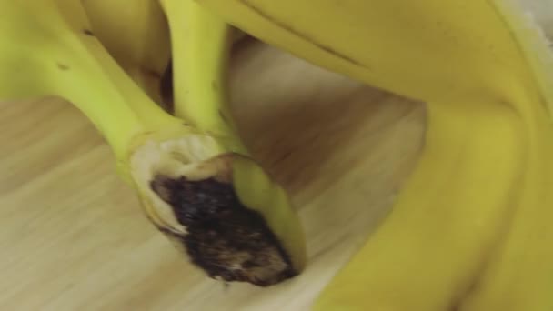 Banda świeżych żółtych bananów i obranego banana obraca się na drewnianym talerzu. — Wideo stockowe