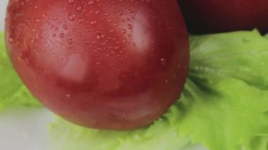 Olgun kırmızı domatesler ve çiğ damlaları beyaz bir tabakta dönen taze yeşil marul.