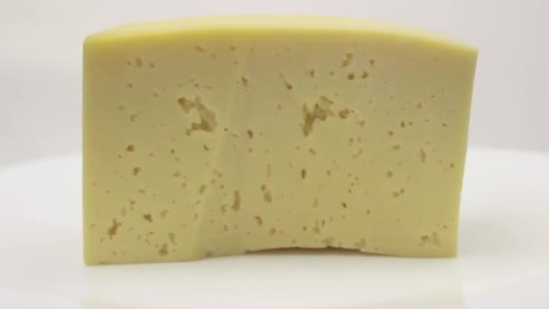 Pedaço de queijo amarelo em um prato de porcelana branca gira em um fundo branco — Vídeo de Stock