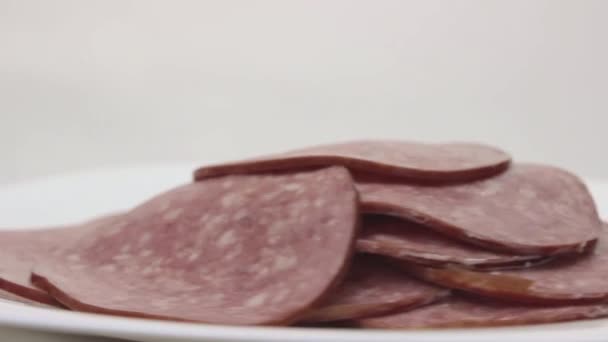 Pile of sliced salami rotates on a white porcelain dish. Smoked sausage slices. — Stock Video