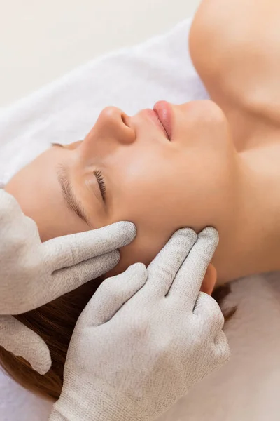 Kozmetik kliniğinde rahatlamış bir kadını yakından çek. Özel eldivenlerle mikro akım terapisi alıyor. Yüz bakımı.