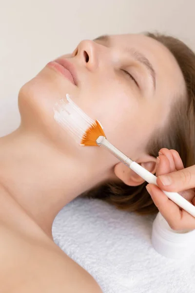 Yüz bakımı. Güzellik uzmanı spa salonunda fırça kullanarak yüzüne maske takıyor. Güzellik kliniğinde kadın müşterinin susuz kalma işlemine yaklaşıyoruz. Kozmetoloji.