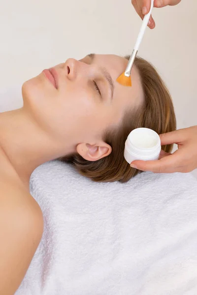 Yüz bakımı. Güzellik uzmanı spa salonunda fırça kullanarak yüzüne maske takıyor. Güzellik kliniğinde kadın müşterinin susuz kalma işlemine yaklaşıyoruz. Kozmetoloji.