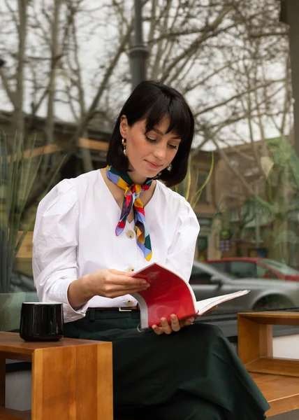 Genç bayan dışarıda oturuyor ve defteri okuyor.