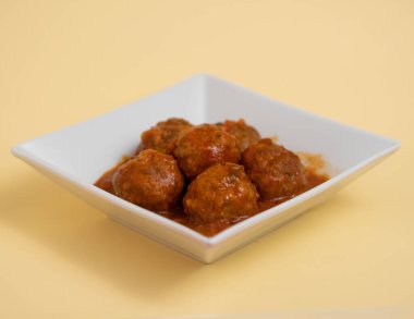 Kare beyazı bir çanak çömlek üzerinde lezzetli köfteler, üzerinde maydanoz yaprakları olan, kremalı bir arka plan.