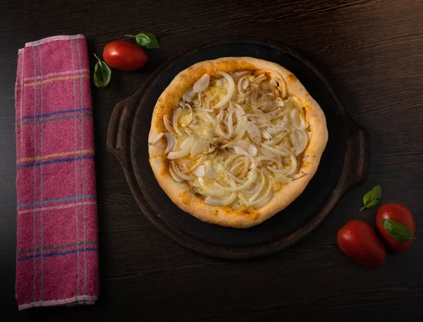 Delicious fried onion pizza accompanied with a glass of cold beer and some tomatoes and a leaf of basil on a wooden table.