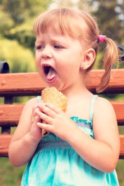 gülümseyen güzel neşeli kız (zevk, ısı - kavram) parkta bankta dondurma yiyor. Vintage tarzı, pastel renkler.