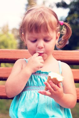 güzel neşeli kız dondurma ve (zevk, ısı - kavram) parkta bankta bir parmak emme yiyor. Vintage tarzı, pastel renkler.