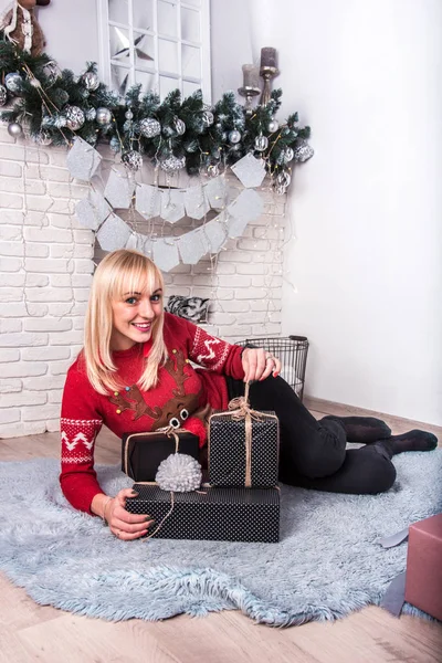 Młoda, atrakcyjna uśmiechnięta kobieta z prezentem świątecznym przy kominku — Zdjęcie stockowe