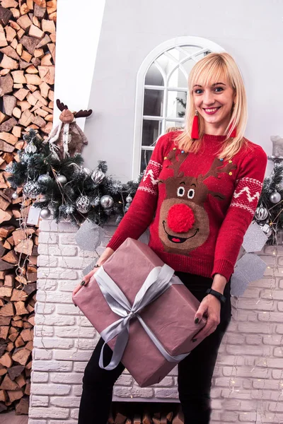 Młoda, atrakcyjna uśmiechnięta kobieta z prezentem świątecznym przy kominku — Zdjęcie stockowe