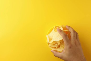 Adamın elinde sarı bir kase vardı. Fast food 'un içinde çıtır patates cipsi vardı. Tuzlu bir tadı var. Enerji, kalori, enerji ve yüksek karbonhidrata sahip. Resim üst görünüm düzlüğü kopyalama alanı ile yatıyordu.
