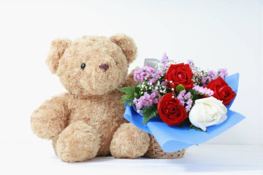 Beyaz arka planda, beyaz ahşap üzerinde güzel güller buketi olan kahverengi oyuncak ayı. Uzay konsepti sevgililer gününü kopyala.