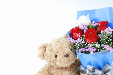 Beyaz arka planda, beyaz ahşap üzerinde güzel güller buketi olan kahverengi oyuncak ayı. Uzay konsepti sevgililer gününü kopyala.