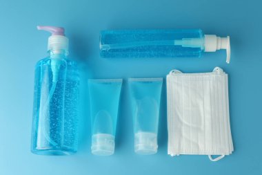Alkol jeli şişeleri, beyaz tıbbi maskeli el dezenfektanı ve mavi arka plan manzaralı düz bir zemin. Bu jel temizleyiciler antibakteriyel ve virüs hijyen için..