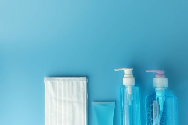 Alkol jeli şişeleri, beyaz tıbbi maskeli el dezenfektanı ve mavi arka plan manzaralı düz bir zemin. Bu jel temizleyiciler antibakteriyel ve virüs hijyen için..