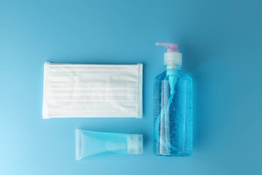Alkol jeli şişeleri, beyaz tıbbi maskeli el dezenfektanı ve mavi arka plan manzaralı düz bir zemin. Bu jel temizleyiciler antibakteriyel ve virüs hijyen için..