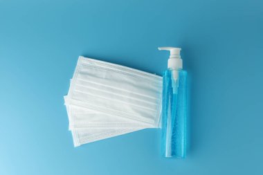 Alkol jeli şişesi, beyaz tıbbi maskeli el dezenfektanı ve mavi arka planda düz bir zemin. Bu jel temizleyiciler antibakteriyel ve virüs hijyen için..
