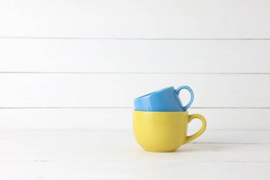 Mavi ve sarı kahve fincanları beyaz ahşap arka planda, fotokopi sapıyla istiflenmiş..