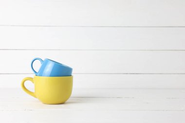 Mavi, sarı kahve fincanları beyaz ahşap arka planda, fotokopi sapıyla istiflenmiş..
