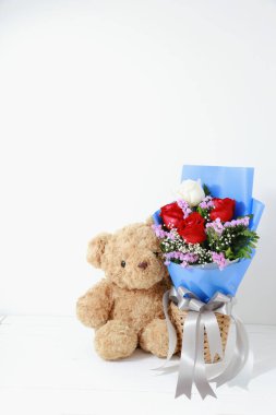 Beyaz arka planda, beyaz ahşap üzerinde güzel güller buketi olan kahverengi oyuncak ayı. Uzay konsepti sevgililer gününü kopyala.