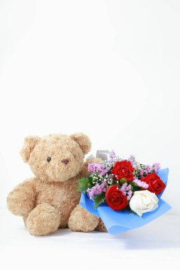 Beyaz arka planda, beyaz ahşap üzerinde güzel güller buketi olan kahverengi oyuncak ayı. Uzay konsepti sevgililer gününü kopyala.