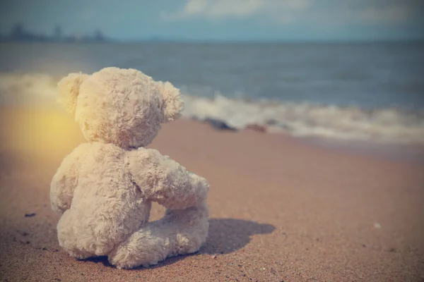 Single teddy bear sitting on the beach alone look on the sea. Image vintage style with copy space.