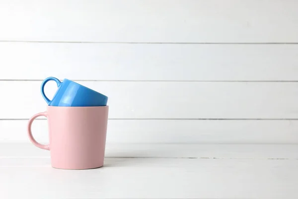 Stacked blue and pink coffee mugs on white wood background.