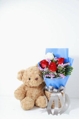 Beyaz arka planda, beyaz ahşap üzerinde güzel güller buketi olan kahverengi oyuncak ayı. Uzay konsepti sevgililer gününü kopyala.