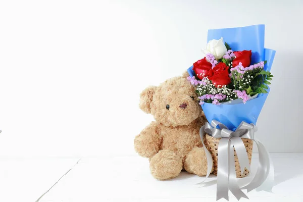 Beyaz arka planda, beyaz ahşap üzerinde güzel güller buketi olan kahverengi oyuncak ayı. Uzay konsepti sevgililer gününü kopyala.