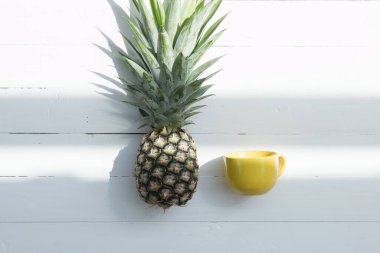 Beyaz arka planda sarı kahve fincanı olan ananas..