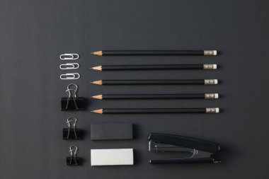 Ofis kırtasiyesi üst görünümü. Kalem, silgi, ataç, zımba, siyah masa düzleştirici ile..