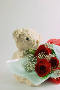Beyaz arka planda oturan oyuncak ayı elinde buket kırmızı güller tutuyor. metin için kopyalama alanı ile. Sevgililer Günü için, bir düğün konsepti.