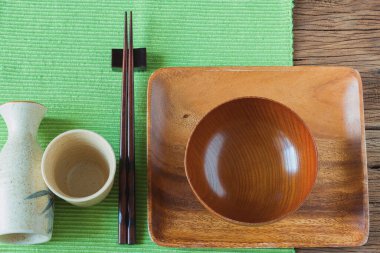 Boş ahşap tabak, kase ve üzerinde yemek çubukları olan sake şişesi. Metin için kopyalama alanı olan üst görünüm.