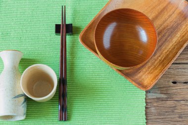 Boş ahşap tabak, kase ve üzerinde yemek çubukları olan sake şişesi. Metin için kopyalama alanı olan üst görünüm.