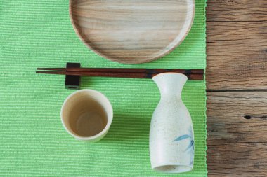 Boş ahşap tabak, masada çubuk olan sake şişesi. Metin için kopyalama alanı olan üst görünüm.