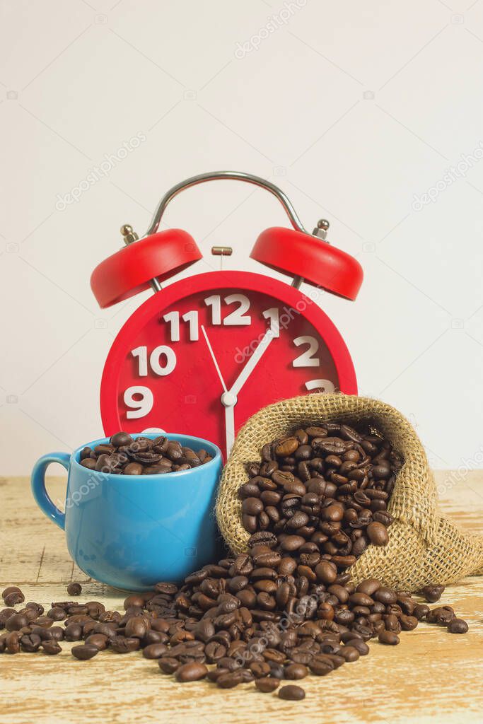 Red alarm clock on the white background wooden table with coffee beans in a sack and blue cup. Copy space for write text.