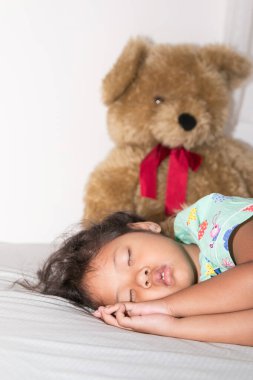Küçük kız, oyuncak ayıyla yatakta uyuyor..