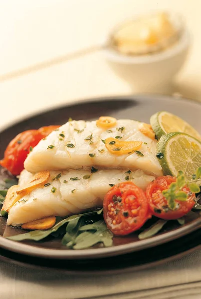 Two Fresh Cod Fillets Cooked Garlic Tomatoes Black Plate Blue — Stock Photo, Image