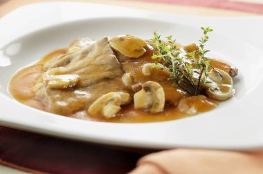 Soslu biftek filetosu ve beyaz tabakta şampiyonlar.