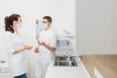 Erkek ve kadın doktorlar medikal modern beyaz ofiste iletişim kurarlar. İki doktor koruyucu maskelerle konuşur. Kapalı
