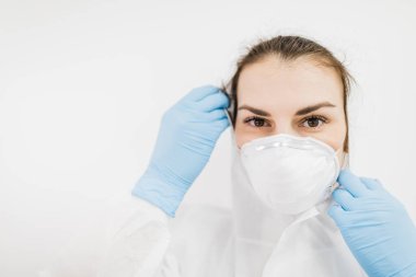 Kız doktor beyaz arka planda mavi eldivenli beyaz koruyucu bir tıbbi maske takıyor..