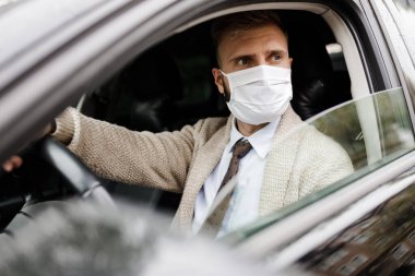 Arabadaki bir adam salgın sırasında maske takıyor. Maskeli bir iş adamı. Virüsten korunuyor. Arabada ceketli bir sürücü. Coronavirus, hastalık, enfeksiyon, karantina, covid-19