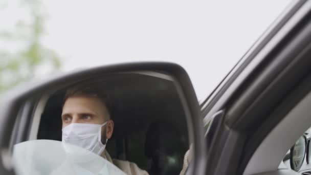 Een man met een medisch masker tijdens een epidemie, een zakenman met een masker, bescherming tegen het virus. Chauffeur in een jasje in een spiegel. Coronavirus, ziekte, infectie, quarantaine, covid-19 — Stockvideo