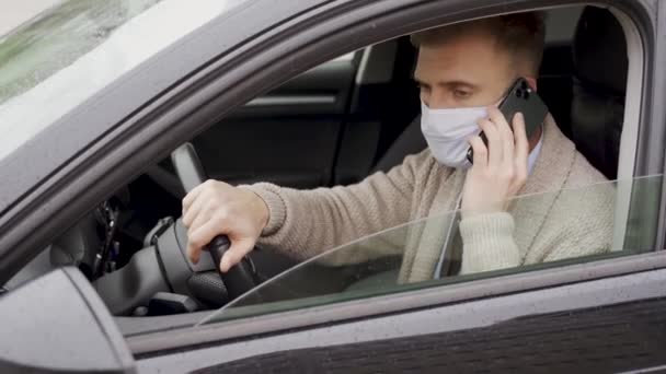 電話で話している車の中で医療マスクの男。流行中のドライバー。ウイルスからの保護。車の中でジャケットのドライバー。コロナウイルス,病気,感染症,隔離, covid-19 — ストック動画