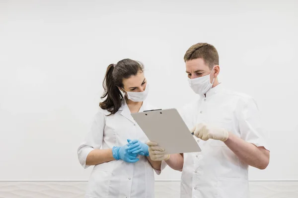 Two doctors talk in protective masks with tablet. Male and female doctors communicate in the medical modern white office. Covid