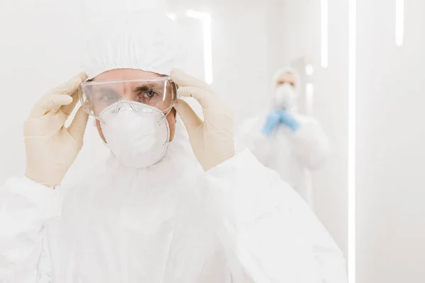 Ein männlicher Arzt zieht seine Schutzmaske während einer Epidemie im weißen Flur des Krankenhauses an. — Stockfoto