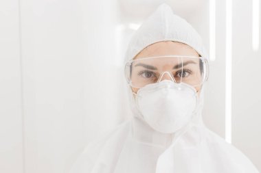 Hastanenin beyaz modern koridorunda salgın sırasında koruyucu kıyafetli bir doktorun kadın portresi..