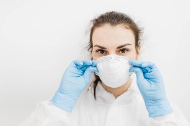 Kız doktor beyaz arka planda mavi eldivenli beyaz koruyucu bir tıbbi maske takıyor..