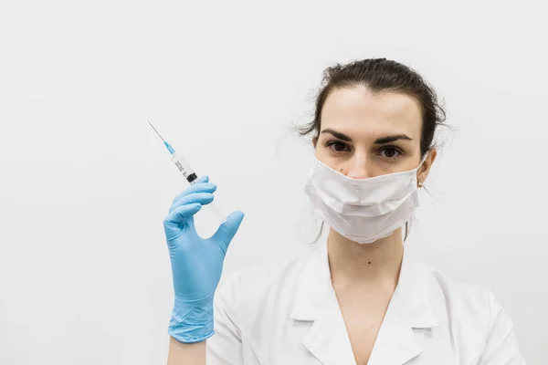 Europejska dziewczyna lekarz w niebieskich rękawiczkach ze strzykawką podczas epidemii w białym pomieszczeniu. — Zdjęcie stockowe